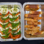 two catering foil containers one with caprese salad and the other one with toast