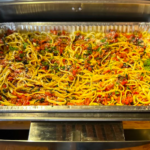 Catering foil tray in rechaud with fettuccini pasta and chopped tomatoes