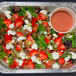 catering foil tray with salad with strawberries goat cheese and walnuts dressing in a round container