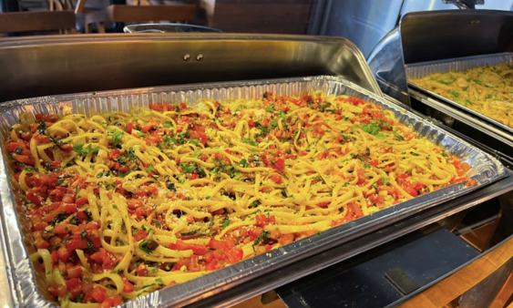 Catering foil tray in rechaud with fettuccini pasta and chopped tomatoes